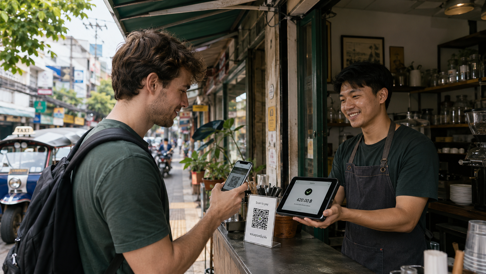 外国人旅行者がバンコクのカフェでQRコードを読み取り、店舗側がバーツ決済端末を確認する様子